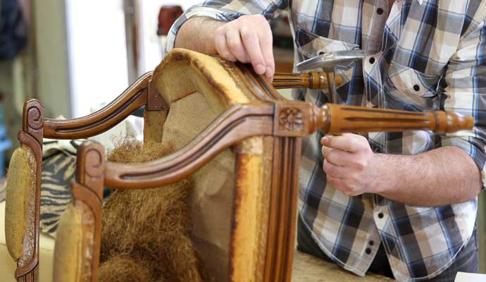 A person working on reupholstering a wooden chair