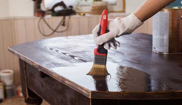 A person varnishing a table using equipment